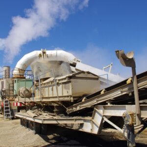 Industrial machinery with a large conveyor system and ducts, set against a blue sky, used for processing materials outdoors.