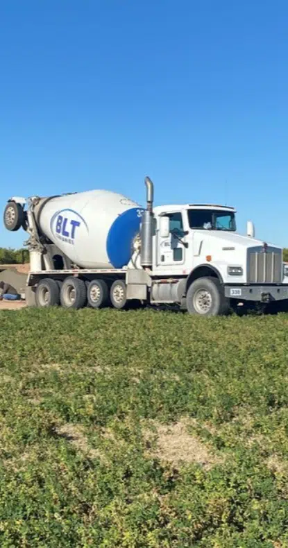 A white cement mixer truck with "BLT" logo is parked on a grassy field under a clear blue sky. A white cement mixer truck with "BLT" logo is parked on a grassy field under a clear blue sky.